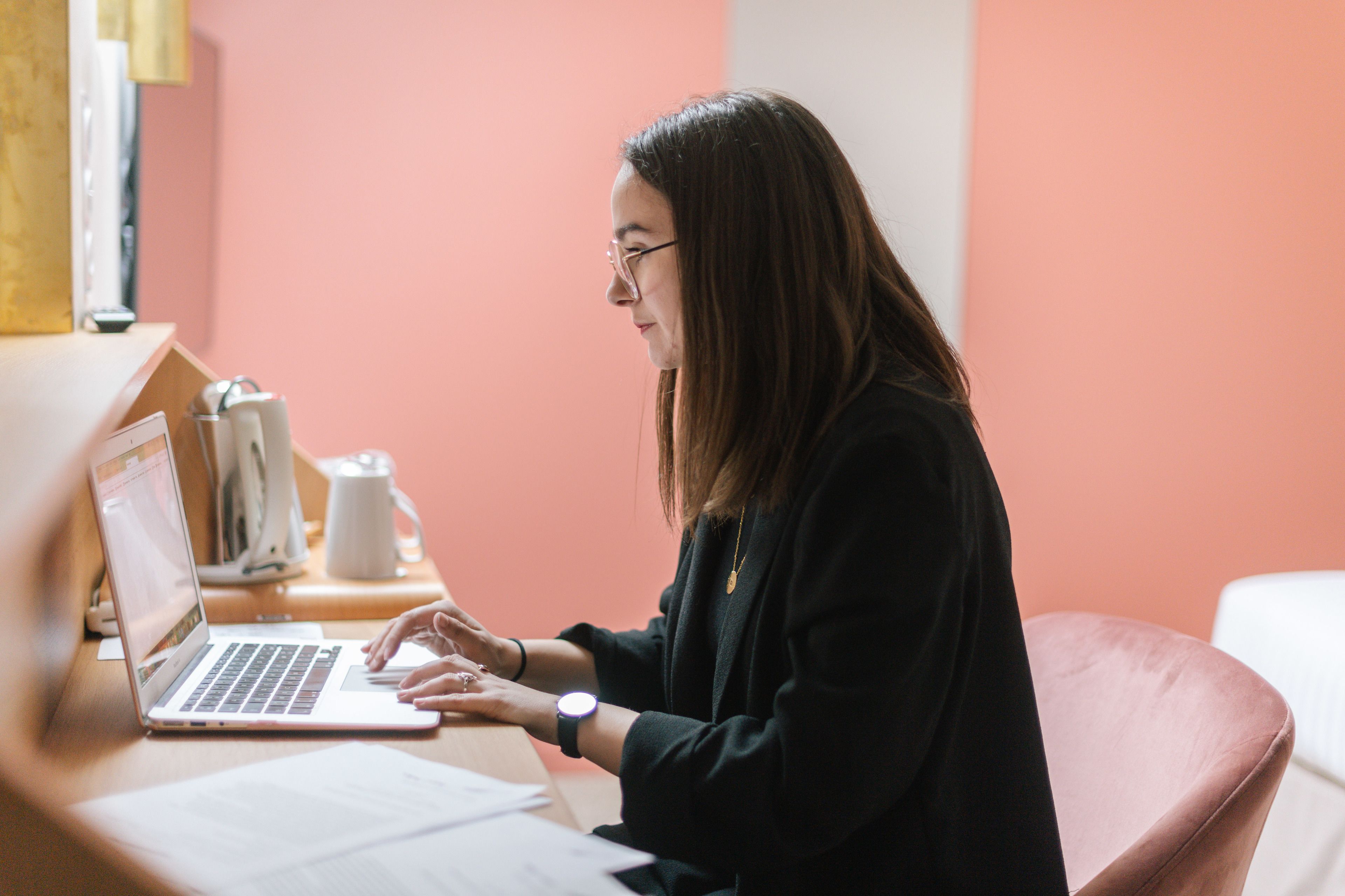 A person using a laptop at a wooden desk with a white mug and a white cup in the background.