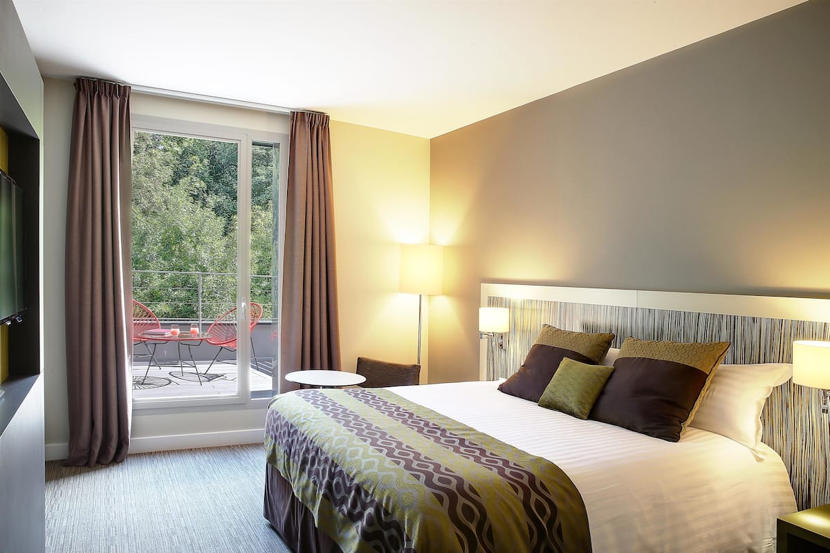 A hotel room with a large bed, a small table, a chair, and a view of the outdoors.