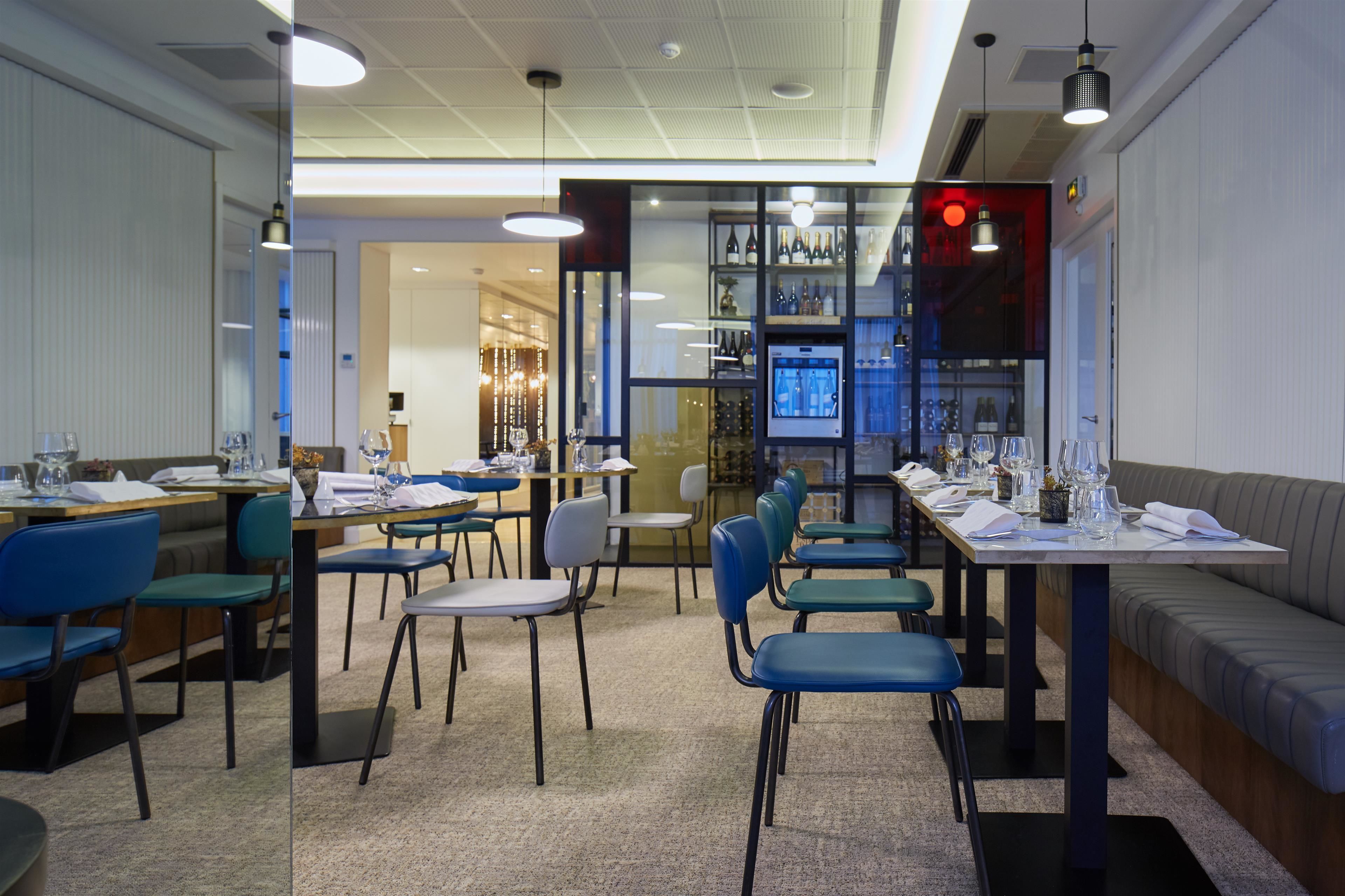 A restaurant with multiple tables and chairs, a bar area with shelves of bottles, and a seating area with a sofa.