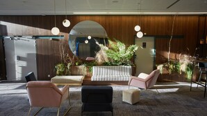 Un espacio de oficina moderno con un espejo grande, paneles de madera y diversas opciones de asientos, incluyendo un sofá y sillas.