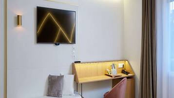 A modern hotel room with a bed, a desk with a chair, a TV mounted on the wall, and a window with curtains.