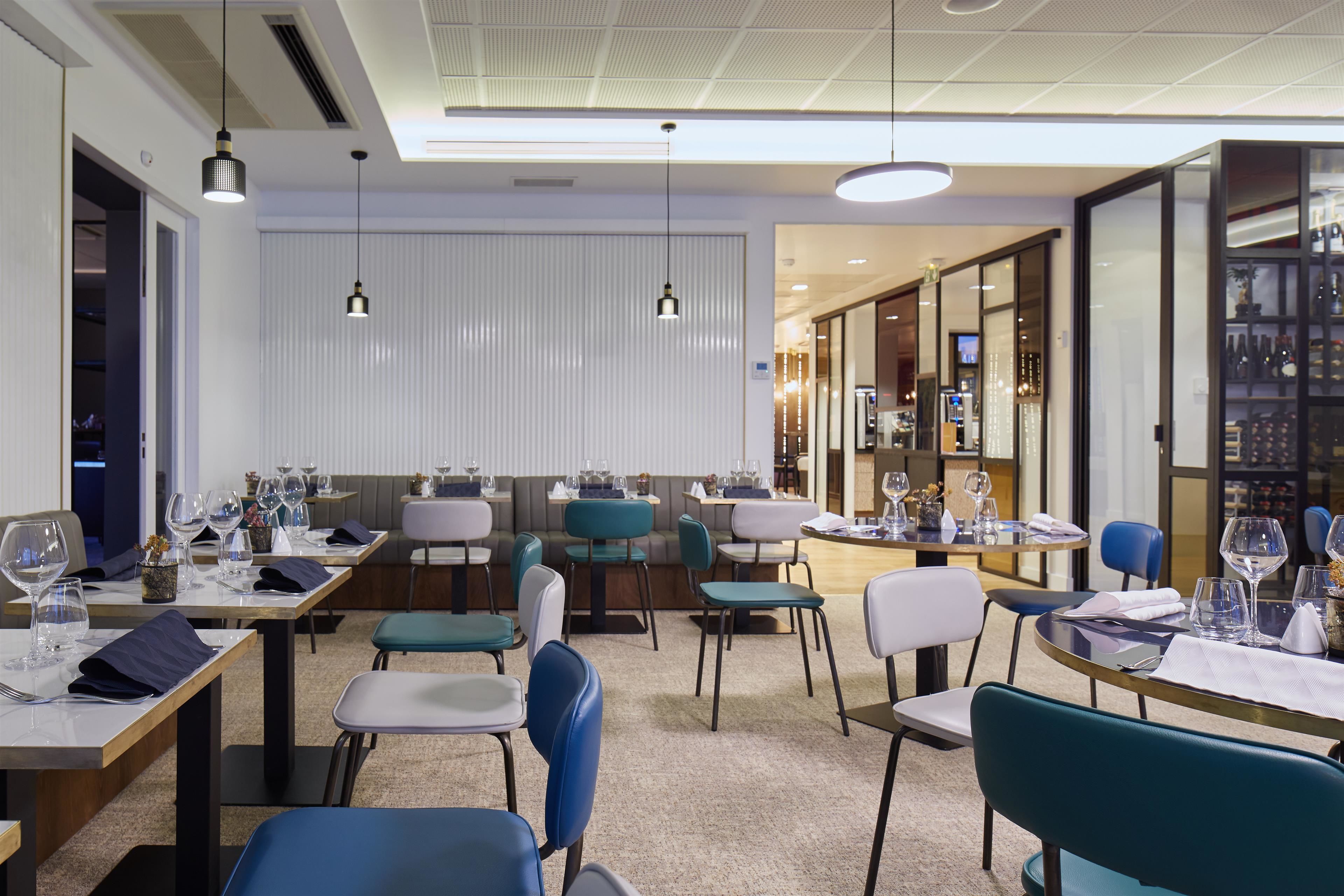 A modern restaurant with multiple tables and chairs, a bar area, and a wine display.