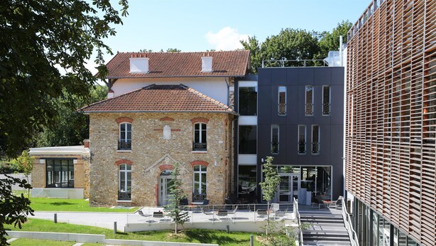 Un edificio moderno con fachada de piedra y tejado de tejas, junto a una estructura contemporánea con fachada de entramado.