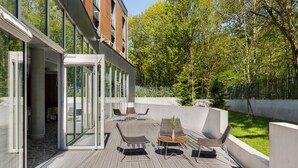 Una terraza moderna al aire libre con puertas de cristal que dan a un patio, amueblada con sillas y una mesa.