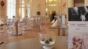 A hotel dining area with clear glass chairs, tables set with white napkins, and a glass bowl with pinecones.