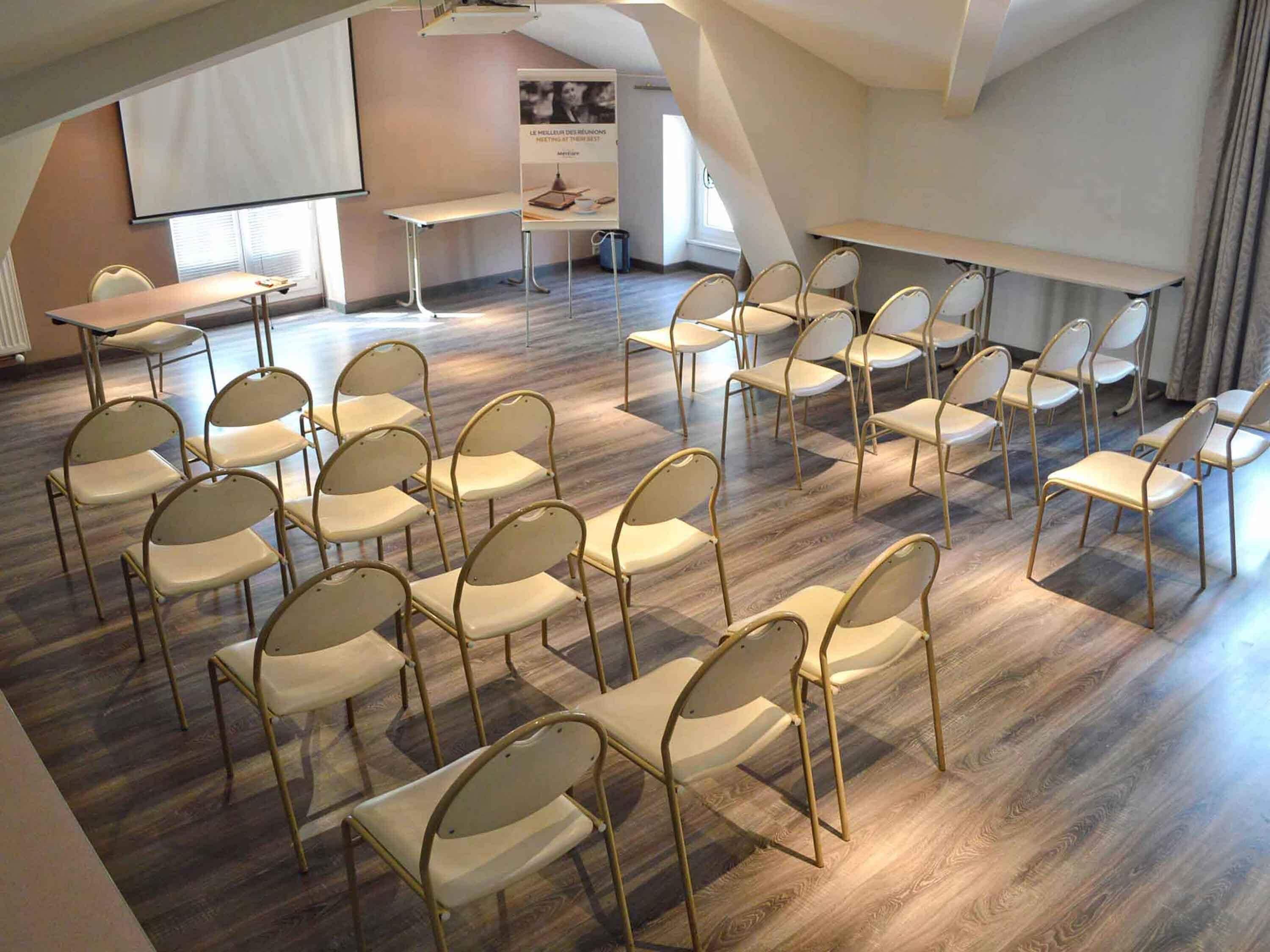 Een vergaderruimte met rijen stoelen, een scherm voor een beamer en een tafel.