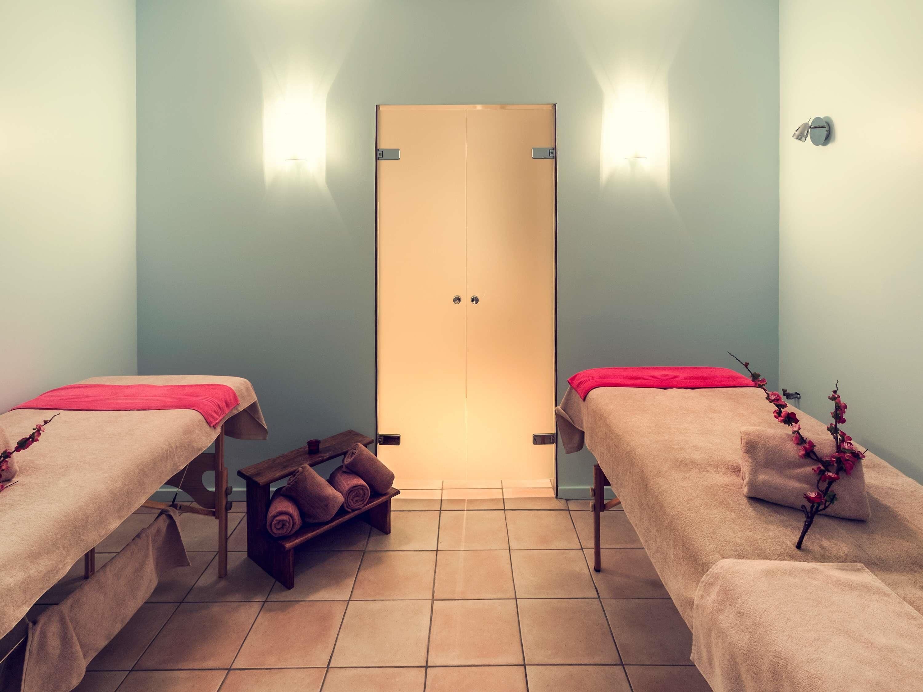 Una habitación con dos camas, un banco de madera con toallas y una puerta con lámpara.