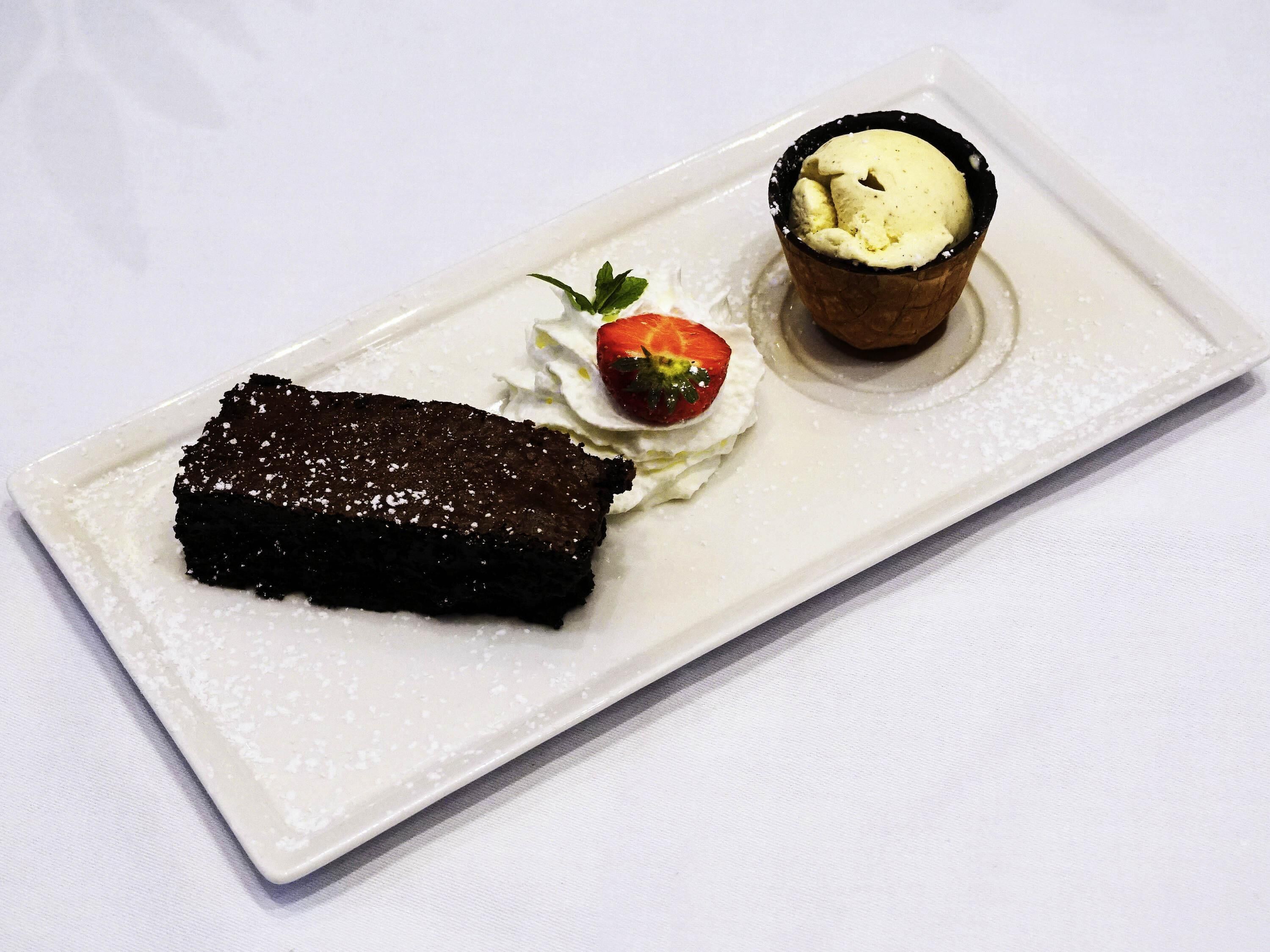 Ein Dessertteller mit Schokoladenkuchen, einer Kugel Eis und einer Erdbeere.