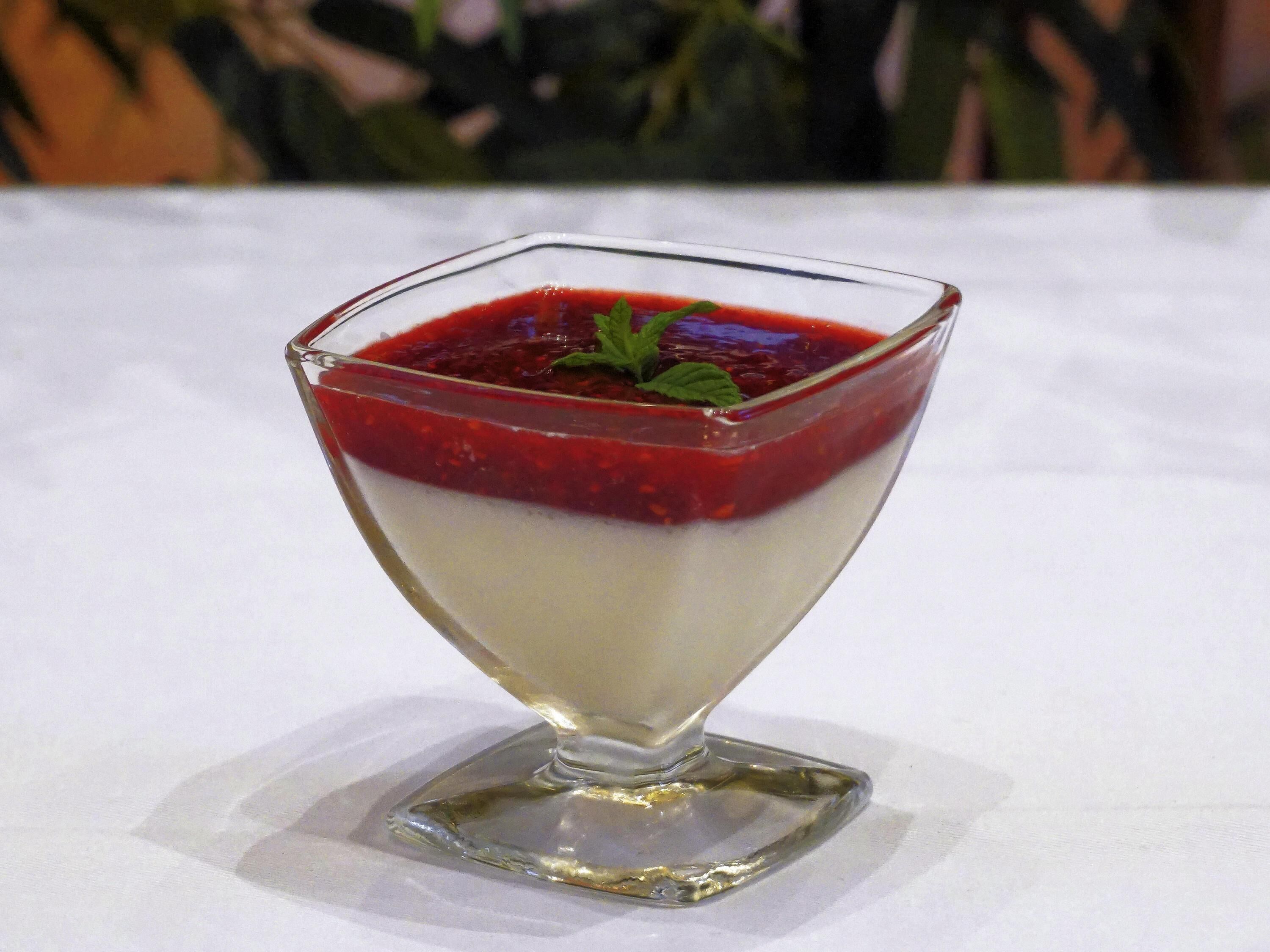 Ein Dessert im klaren Glas mit quadratischem Boden auf weißem Tisch.
