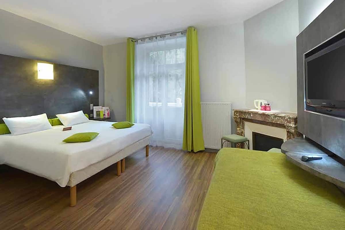 A hotel room with a bed, a TV, a fireplace, and a window with curtains.