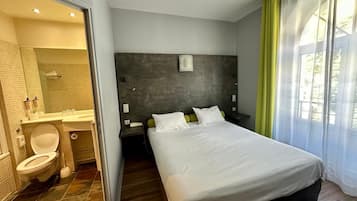Een moderne hotelkamer met een groot bed, een nachtkastje, een badkamer met toilet, wastafel en spiegel.