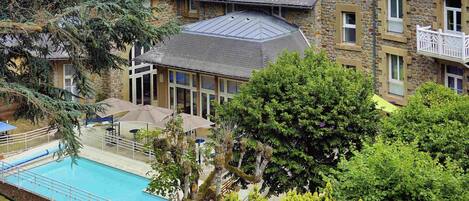 A residential building with a swimming pool, stone facade, and multiple windows.