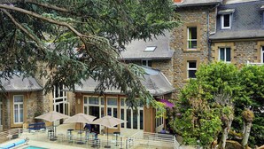 A pool area with lounge chairs and umbrellas, surrounded by stone buildings with large windows.