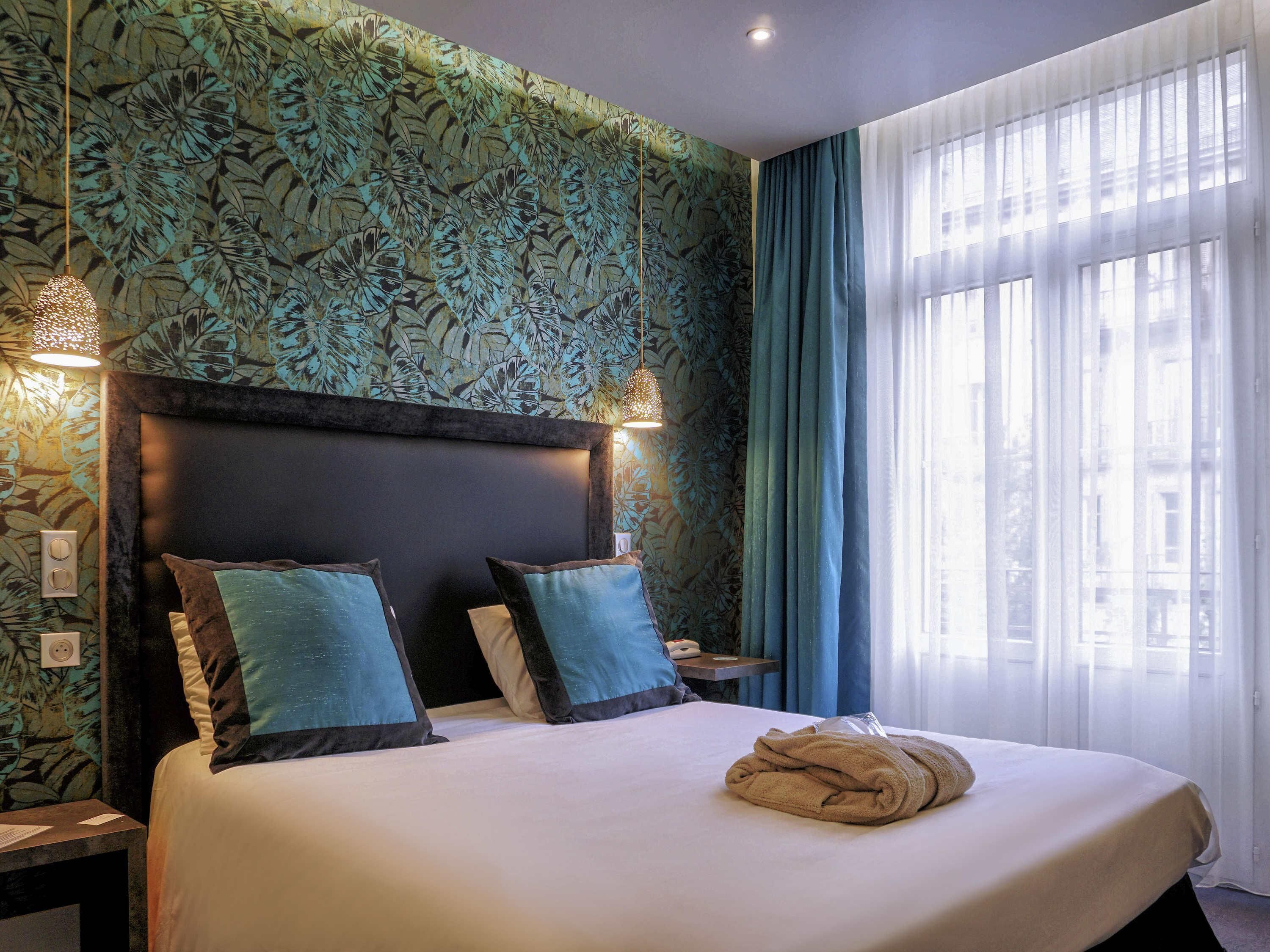 A hotel room with a large bed, a headboard, a nightstand, a lamp, and a window with curtains.