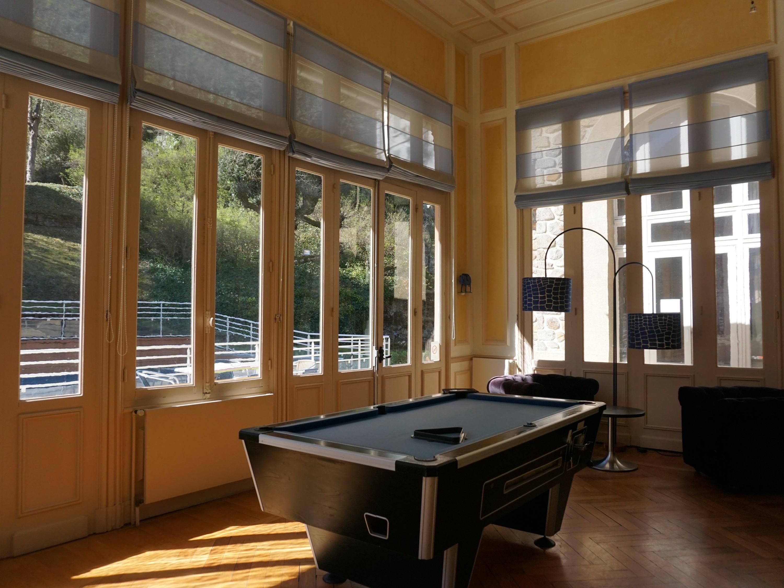 A pool table in a room with large windows, a lamp, and a view of a balcony.
