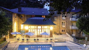 A stone building with a swimming pool, outdoor seating, and a staircase leading to a balcony.