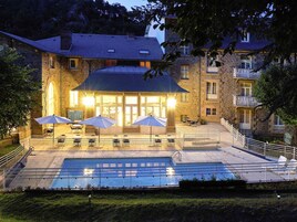 Un edificio de piedra con piscina, zona de estar al aire libre y una escalera que lleva a un balcón.