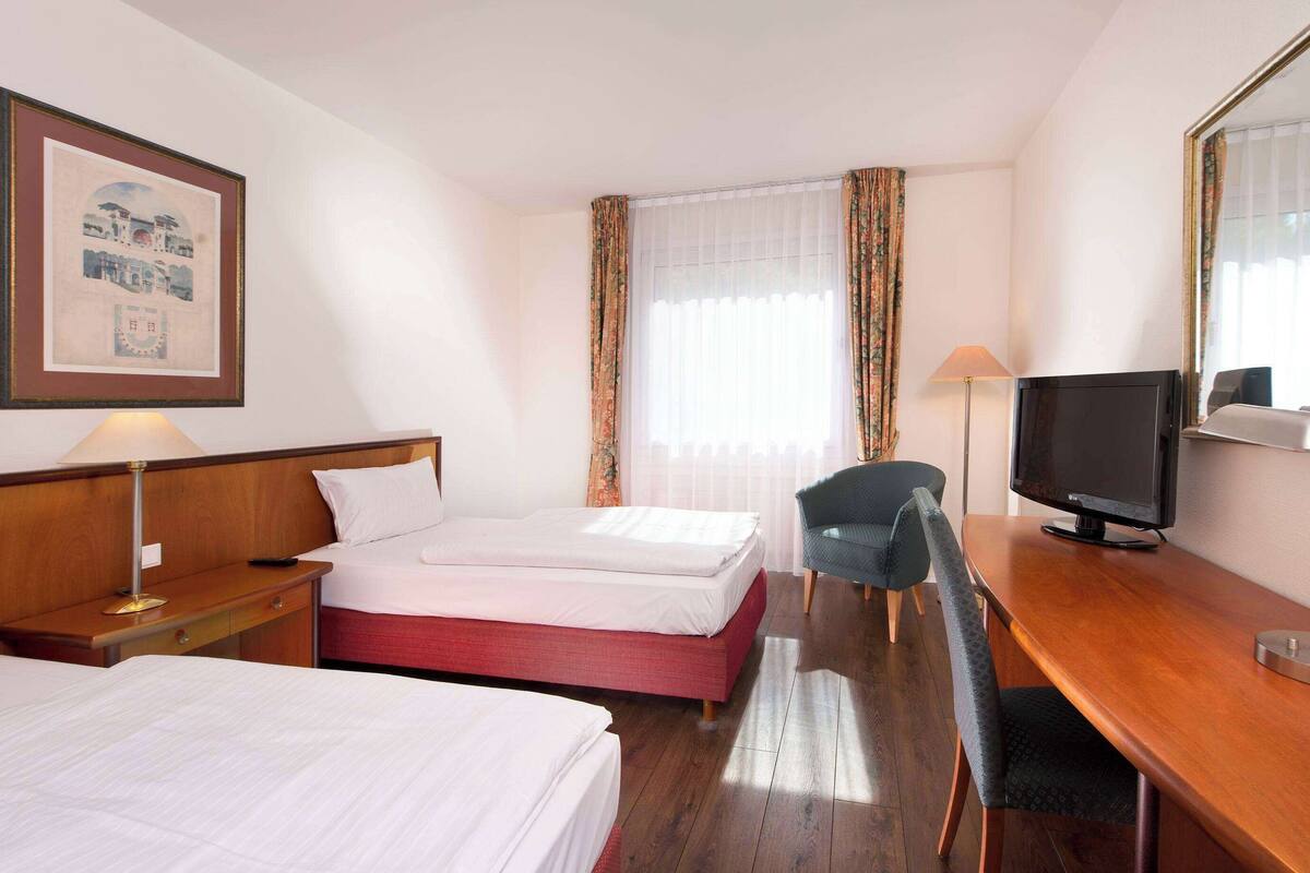 Une chambre d’hôtel avec deux lits, un bureau avec une télévision, une chaise et une lampe.