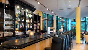 A bar area with a long counter, bar stools, and shelves stocked with glasses and bottles.