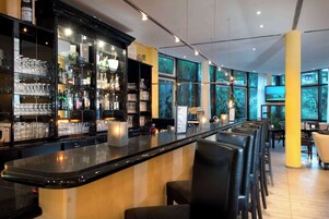 Una zona de bar con una barra larga, taburetes y estantes llenos de copas y botellas.
