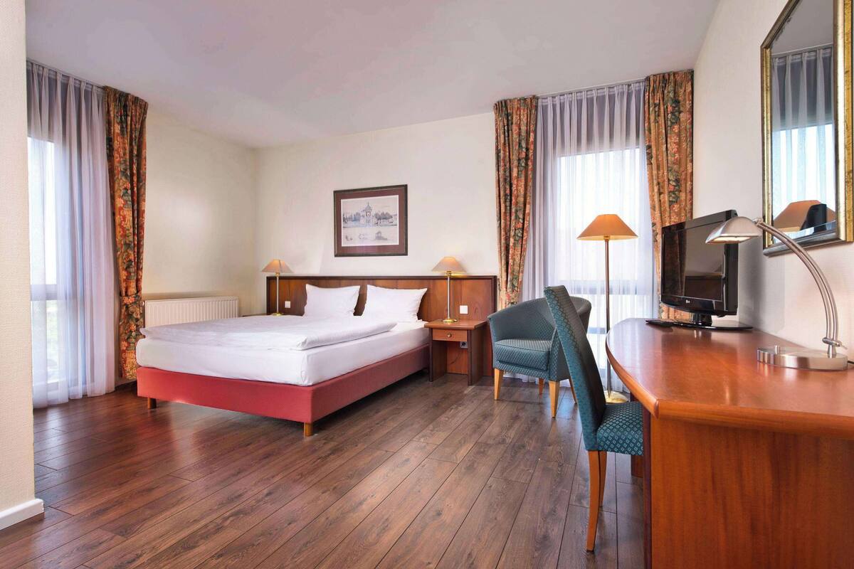 Une chambre d’hôtel avec un lit, un bureau doté d’une lampe, une chaise, un téléviseur et un tableau encadré au mur.