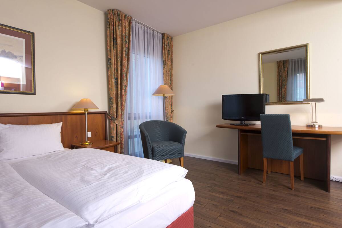 Une chambre d’hôtel comprenant un lit, deux chaises, un bureau avec une télévision et un miroir.