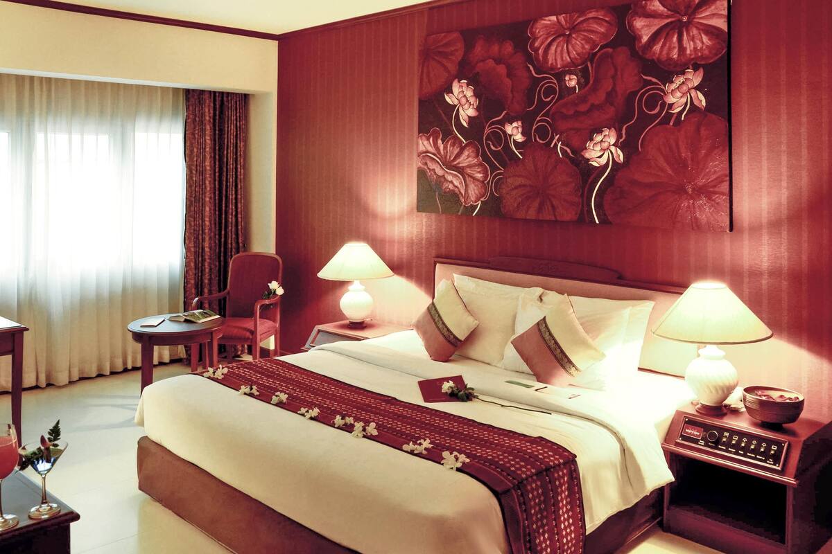A hotel room with a large bed, two bedside tables, a chair, a desk, and a large floral artwork on the wall.