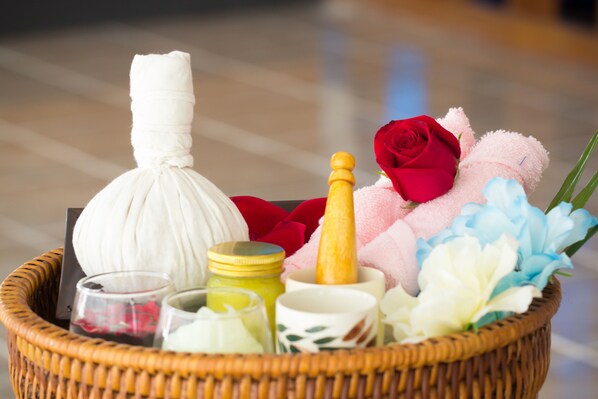 A wicker basket containing a massage stone, a bottle, a red rose, a plush toy, and some flowers. - Mercure Chiang Mai (Chiang Mai)