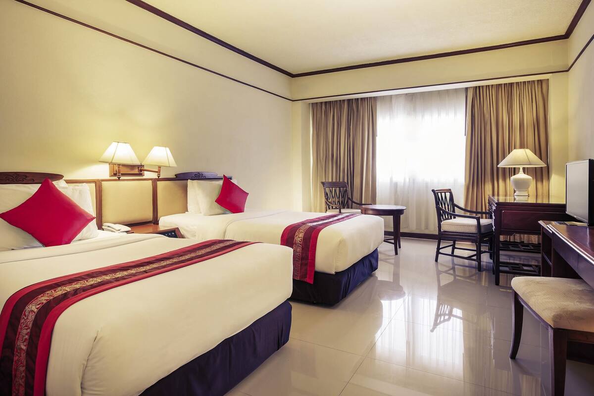 A hotel room with two beds, a desk, a chair, and a television.
