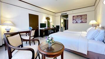 A hotel room with a bed, a desk, two chairs, a small table with a vase of flowers, and a television.