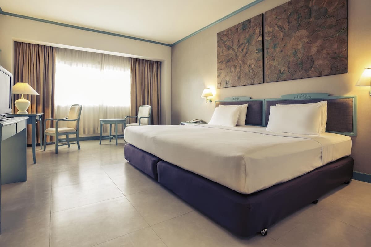 A hotel room with a large bed, a desk, a chair, and a window with curtains.