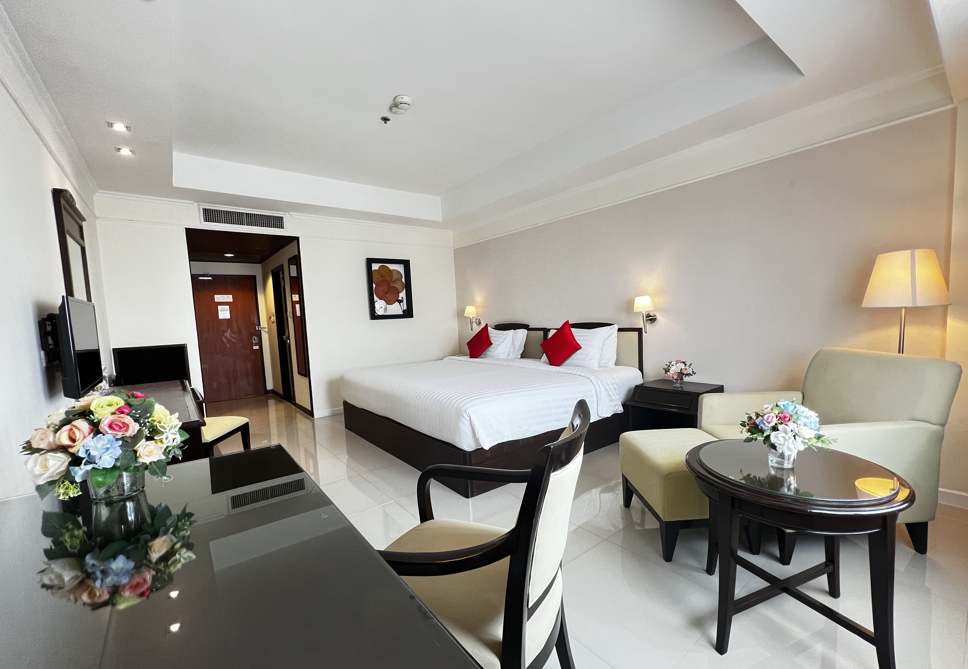 A hotel room with a bed, bedside tables, a desk, a chair, and a round table with a vase of flowers.