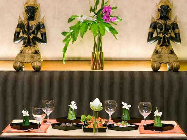 A dining table with a floral centerpiece, two statues, and various dishes and glasses. - Mercure Chiang Mai (Chiang Mai)