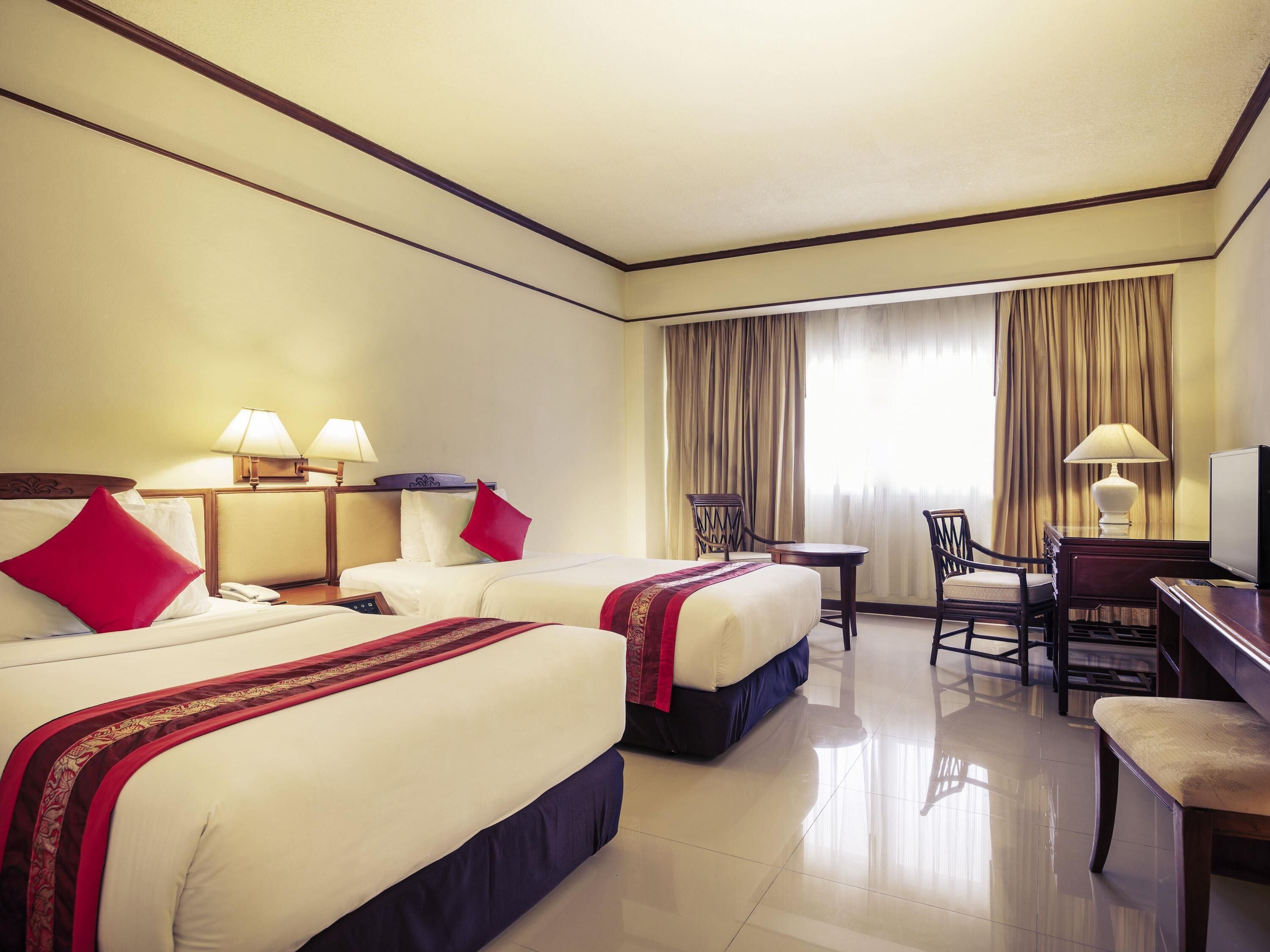A hotel room with two beds, a desk, a chair, and a television.