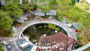 Un espacio al aire libre circular con un estanque, zonas de estar y sombrillas.