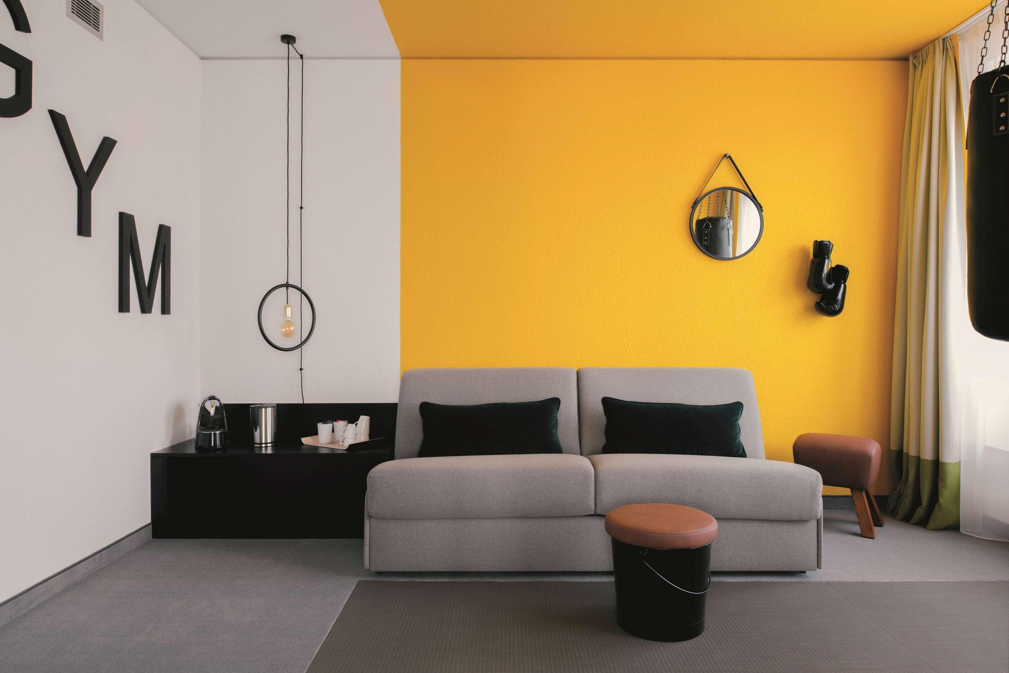 A modern living room with a grey sofa, black and green cushions, a black coffee table, a small black stool, a round mirror, and a punching bag.