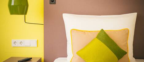 A hotel room with a bed, a nightstand, a green pendant light, and a wall socket.