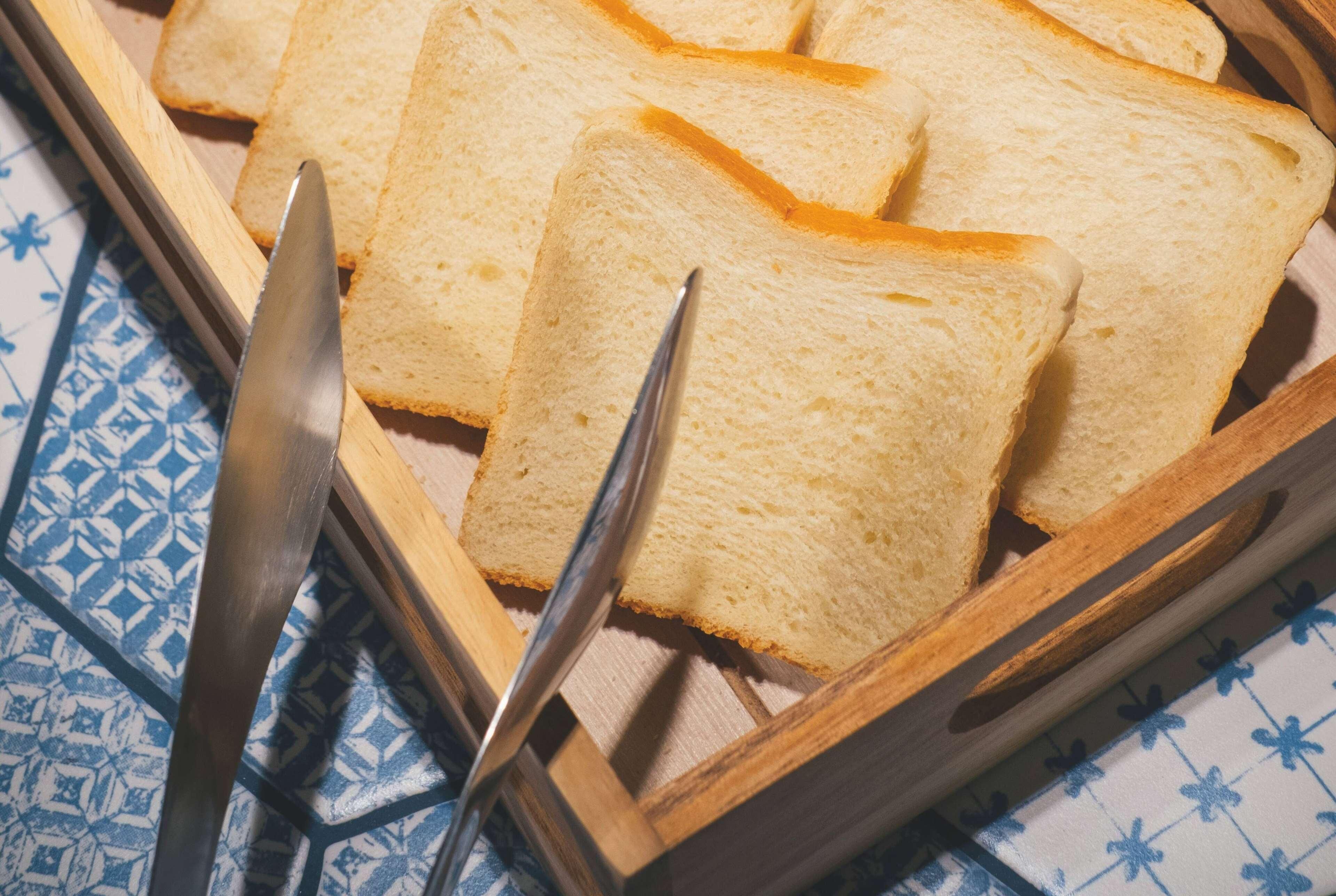 Slices of white bread on a wooden tray with a knife and fork.