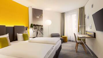 Ein Hotelzimmer mit zwei Betten, einem Schreibtisch, einem Stuhl, einer Lampe und einem großen Fenster mit Vorhängen.