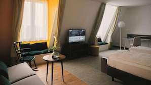 A hotel room with a bed, a TV, a desk, a chair, a sofa, and a window with curtains. - Sunday Hotel Leipzig (Leipzig)