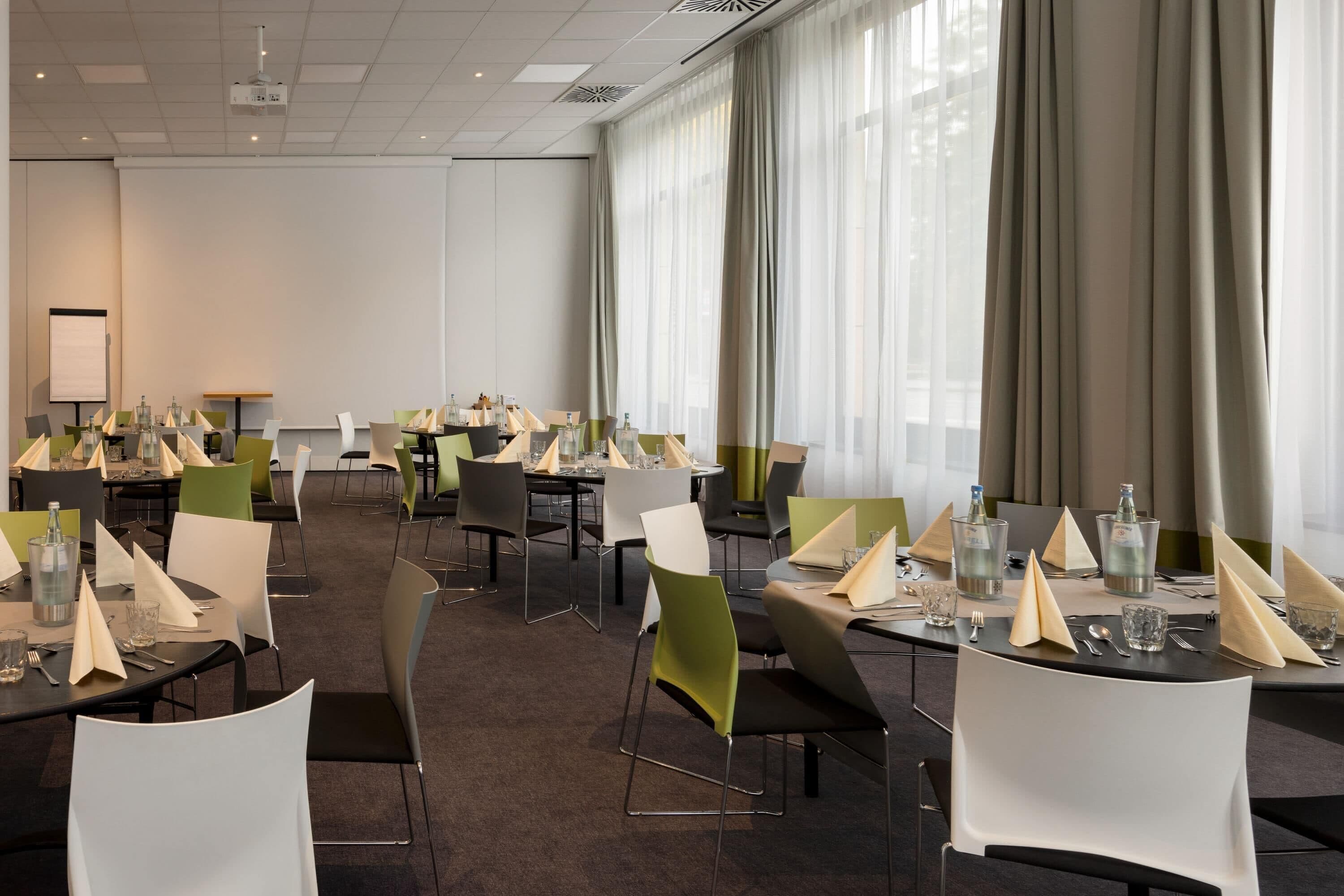 Un salón de conferencias con varias mesas dispuestas para reuniones, equipado con proyectores y pantallas.