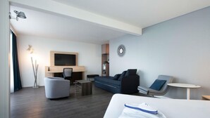 A modern hotel room with a flat-screen TV, a sofa, a desk, and a small table.