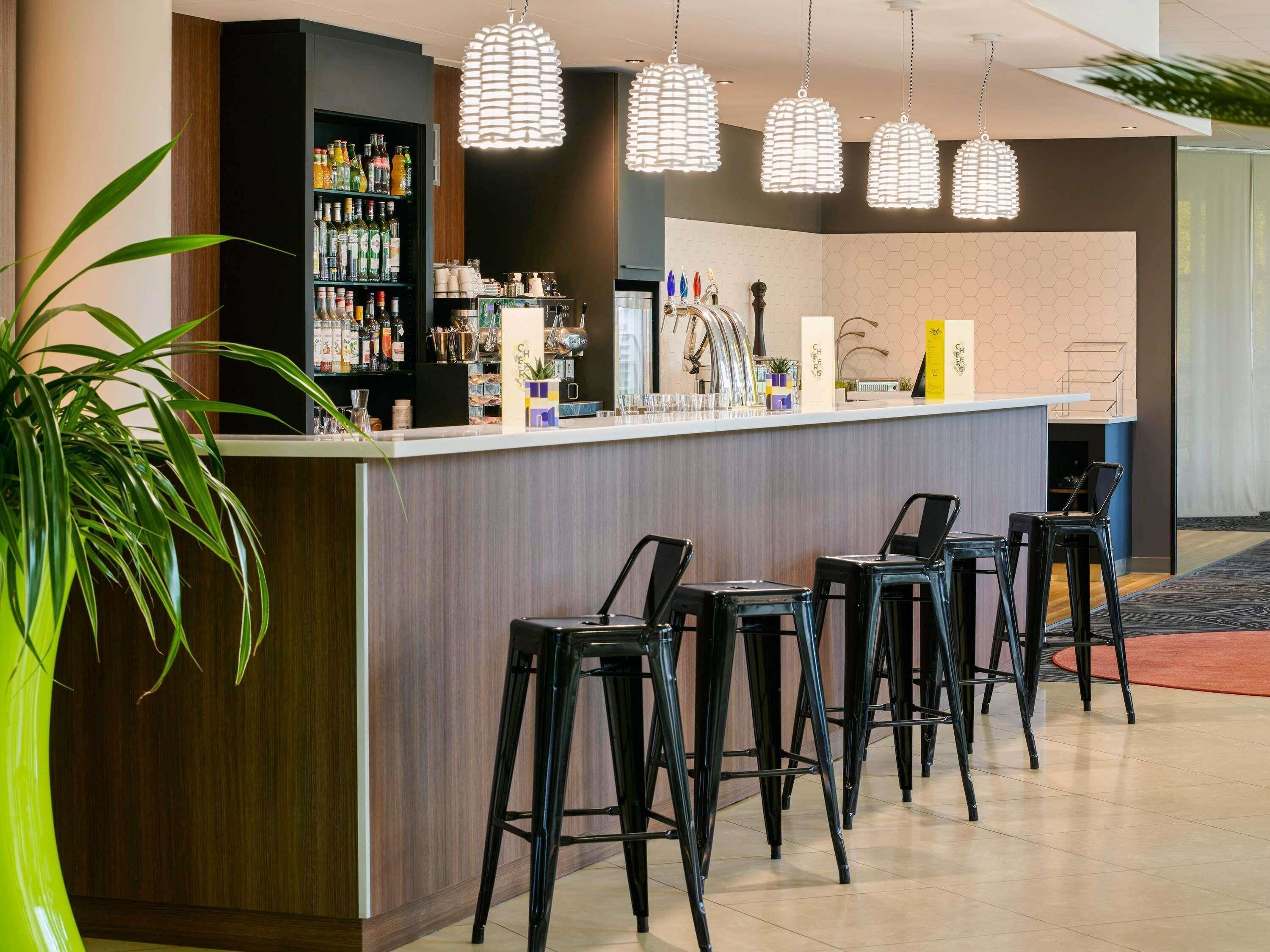 Zona de bar con mostrador, taburetes y una variedad de botellas y vasos.