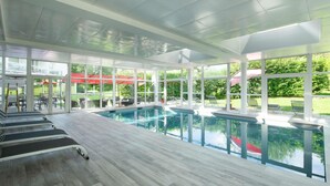 A swimming pool area with clear glass walls, a wooden deck, and outdoor seating.