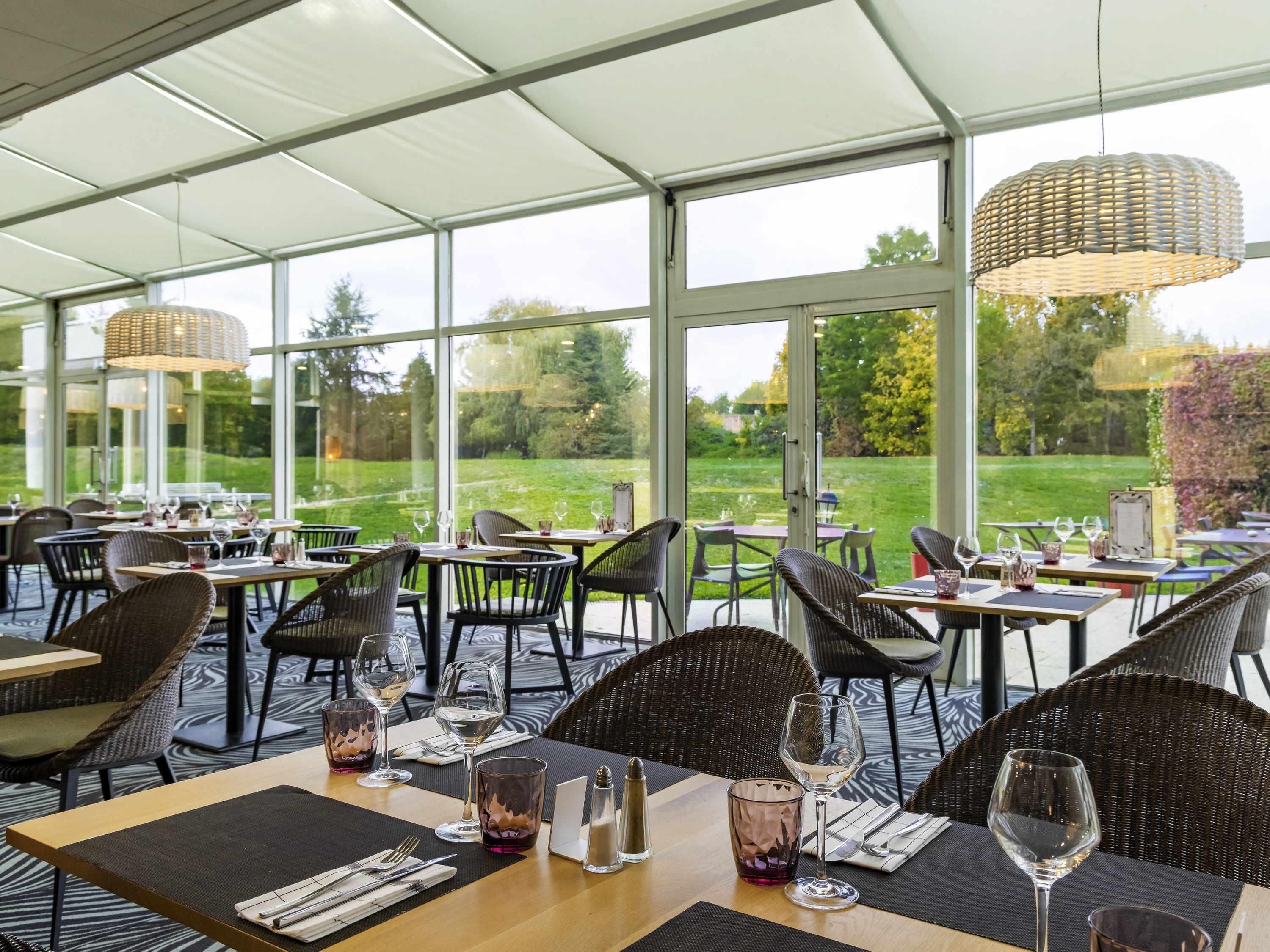 An indoor dining area with tables and chairs, large windows, and a view of a grassy landscape.