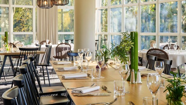 A dining area with tables set for service, large windows, and hanging pendant lights.