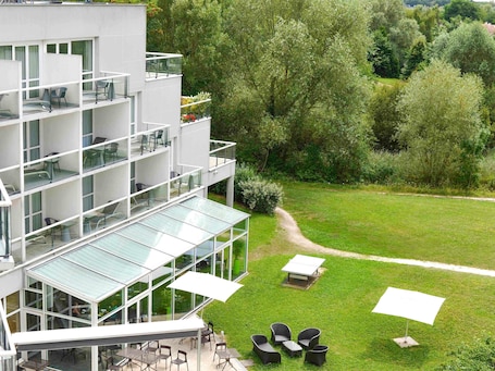 Un bâtiment moderne à plusieurs étages, doté d’une terrasse et d’une véranda en verre.. Hôtel Novotel Senart Golf de Greenparc
