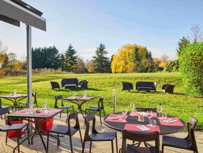 An outdoor dining area with tables and chairs, surrounded by a grassy field and trees.