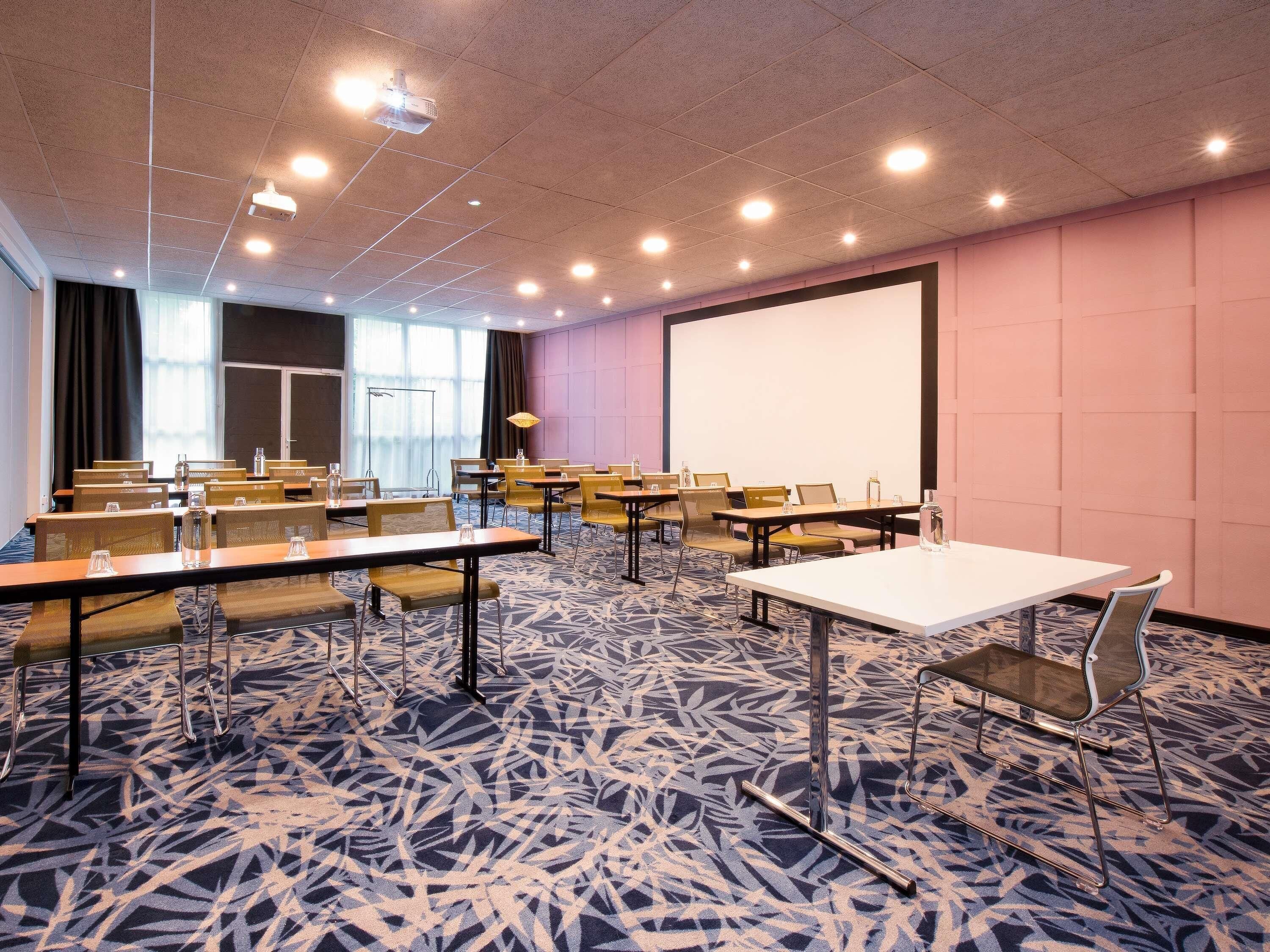 Un salón de conferencias con mesas, sillas, un proyector y una pantalla grande.