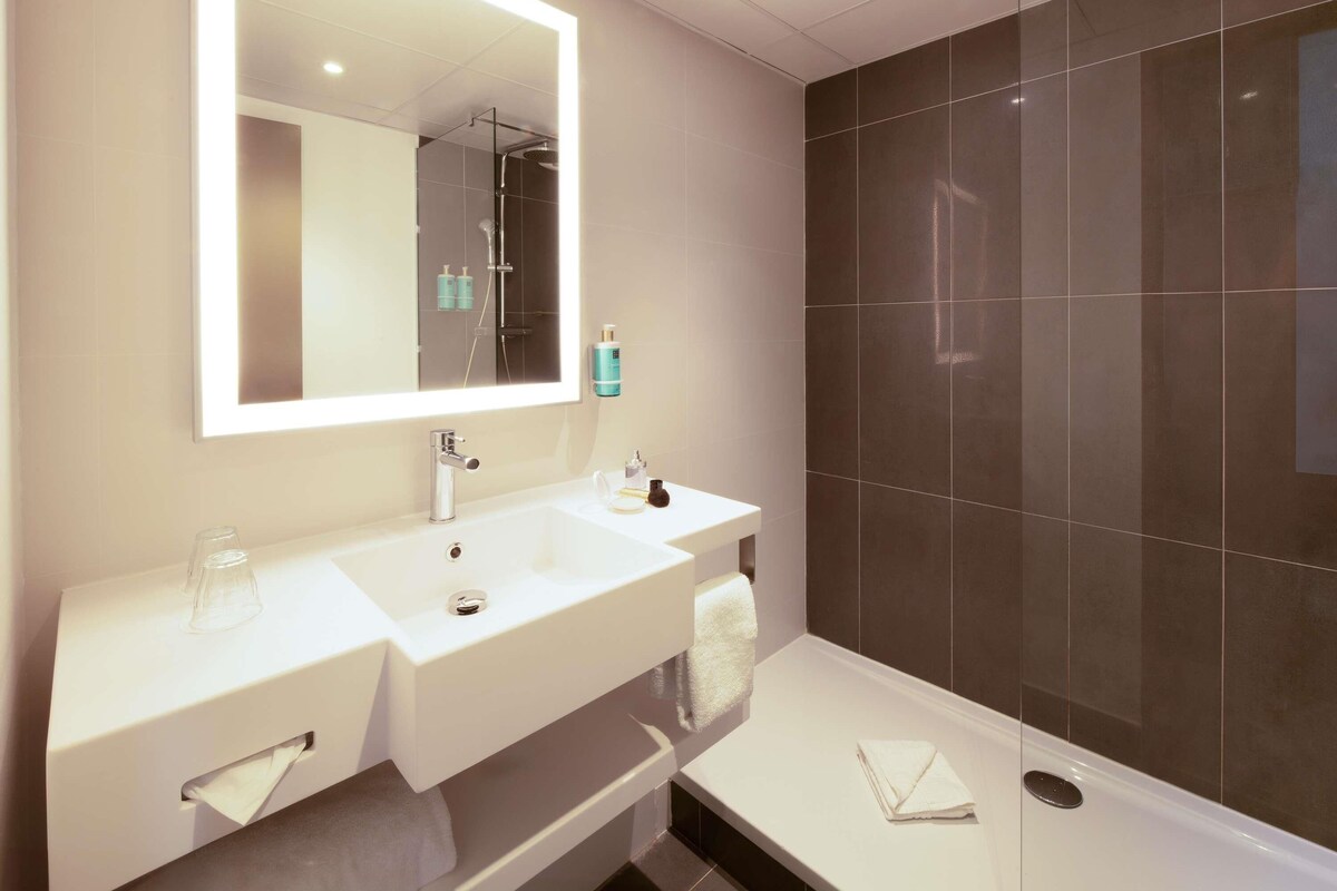 Une salle de bain moderne avec un grand miroir, deux lavabos, une douche et un porte-serviettes.